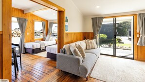 A room with a wooden floor, a grey sofa, a bed, and a sliding glass door leading to an outdoor area. - Punakaiki Beachfront Motels (Punakaiki)