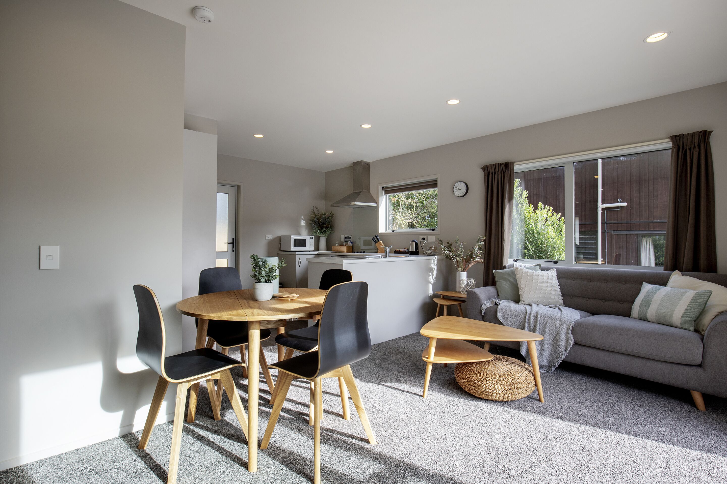 A modern living room with a grey sofa, a dining table with chairs, and a kitchen area in the background.