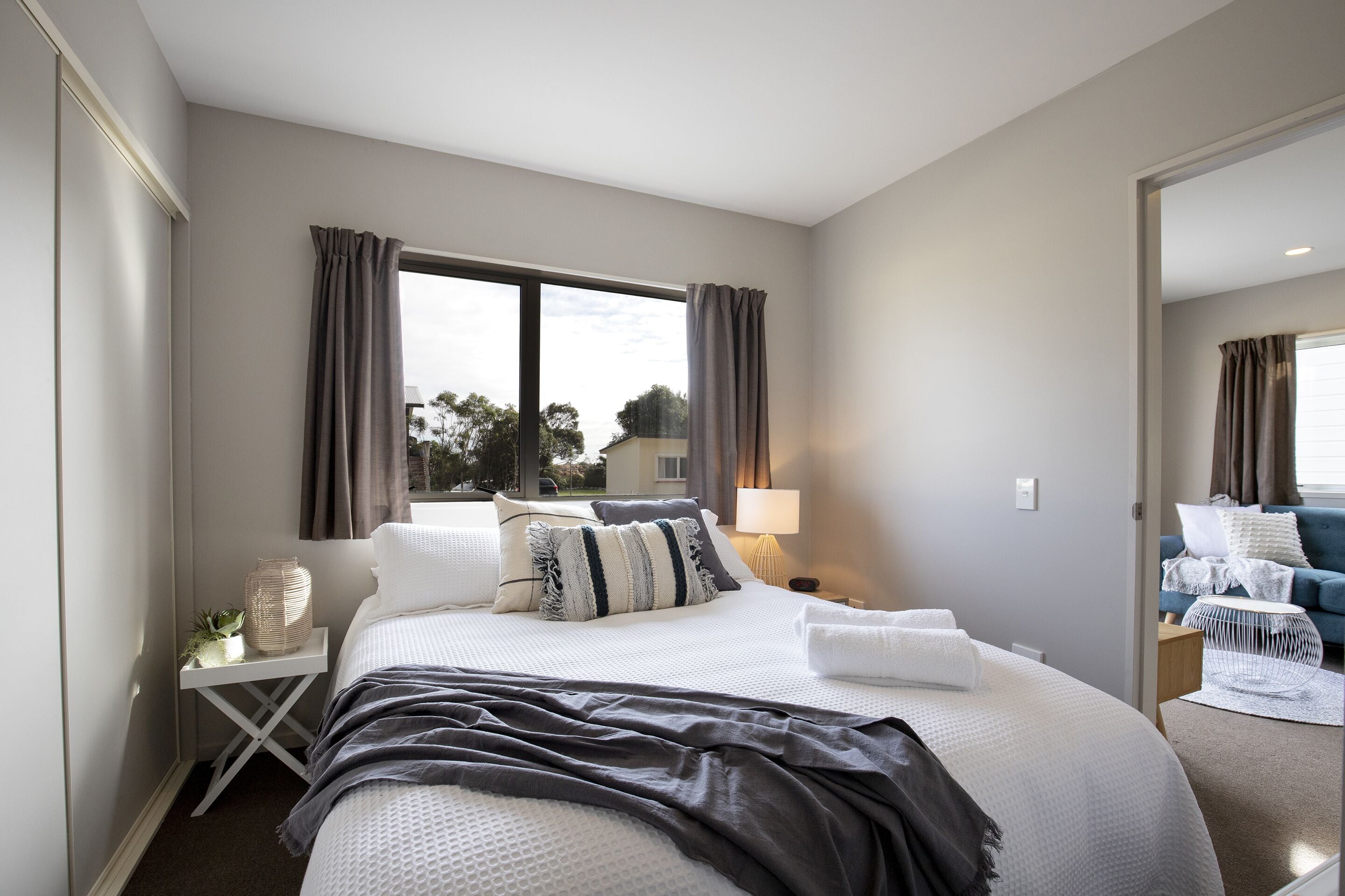 Une chambre d’hôtel moderne avec un grand lit, une table de chevet avec une lampe et une vue sur l’extérieur par une fenêtre.