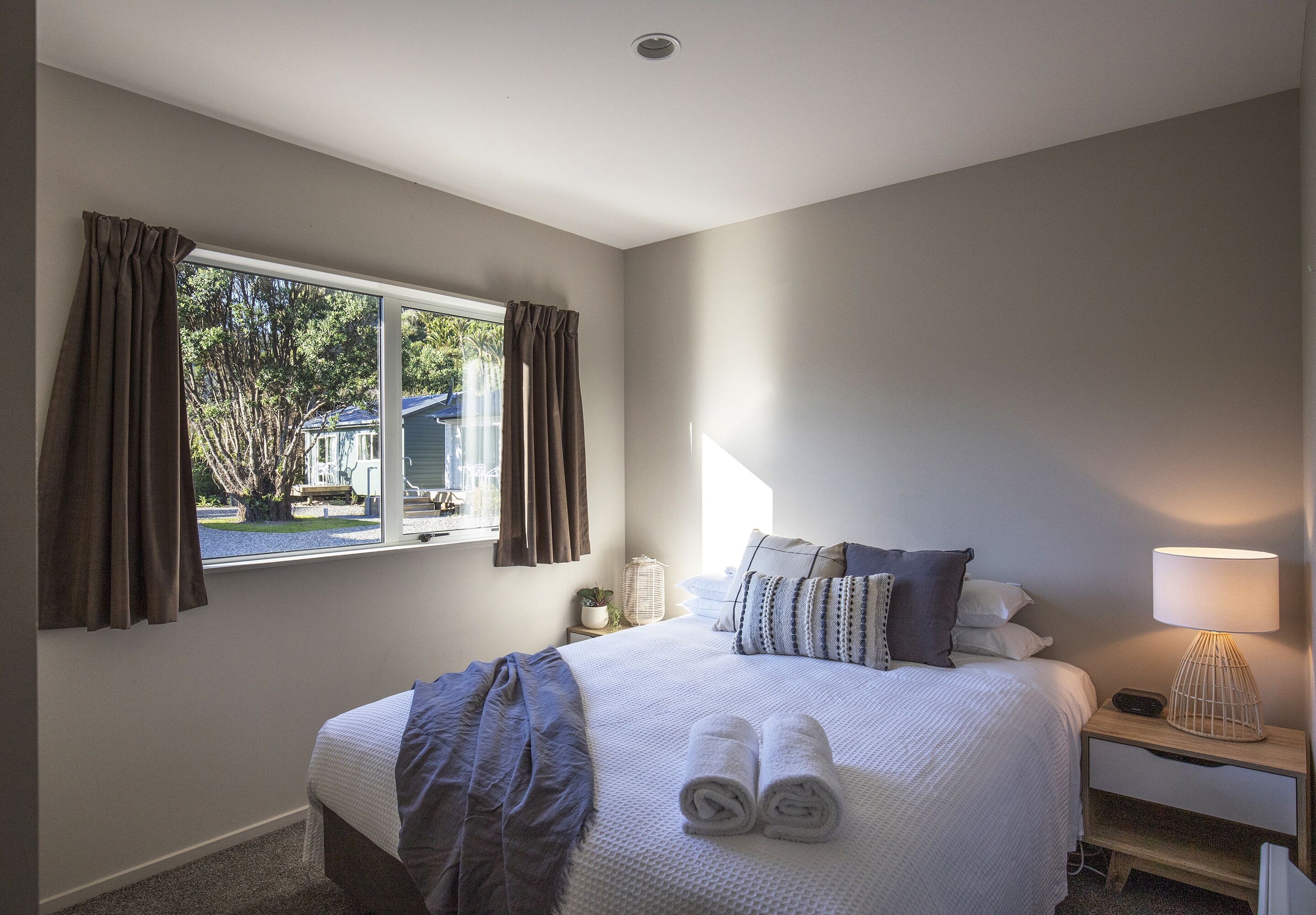 A bedroom with a large bed, a bedside table with a lamp, and a window with curtains.