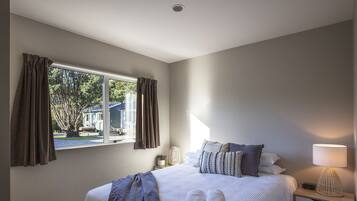 A bedroom with a large bed, a bedside table with a lamp, and a window with curtains.
