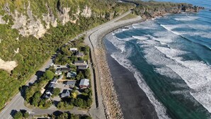 An aerial view of a coastal area with a road curving along the beach, houses adjacent to the road, and cliffs with vegetation. - Punakaiki Beachfront Motels (Punakaiki)