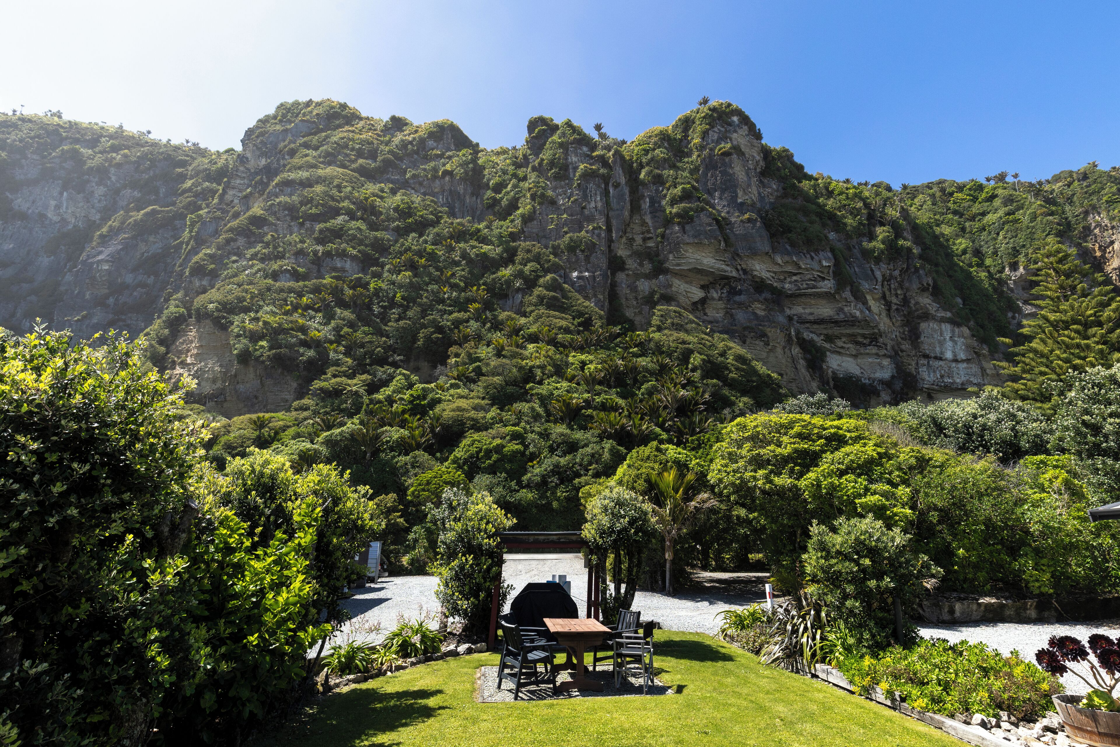 Une terrasse avec un barbecue, entourée d’une végétation luxuriante et avec une chaîne de montagnes en toile de fond.