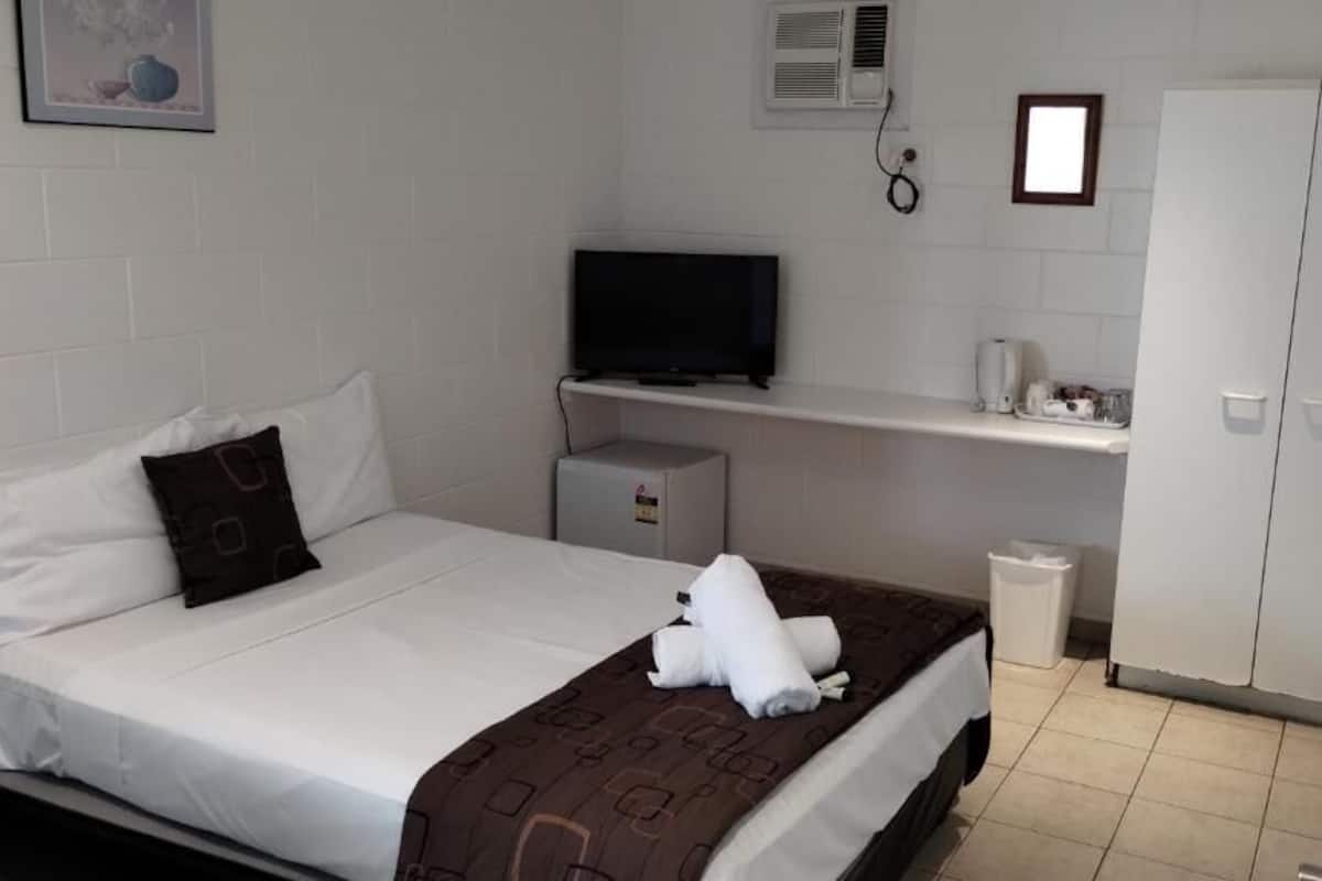 A hotel room with a bed, a television, a small heater, a wardrobe, and a trash bin.