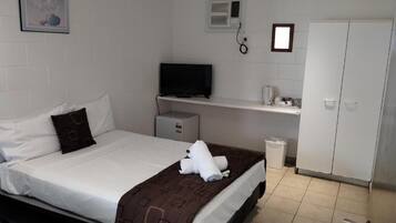 Quarto de hotel com uma cama, televisão, aquecedor pequeno, guarda-roupa e lixeira.