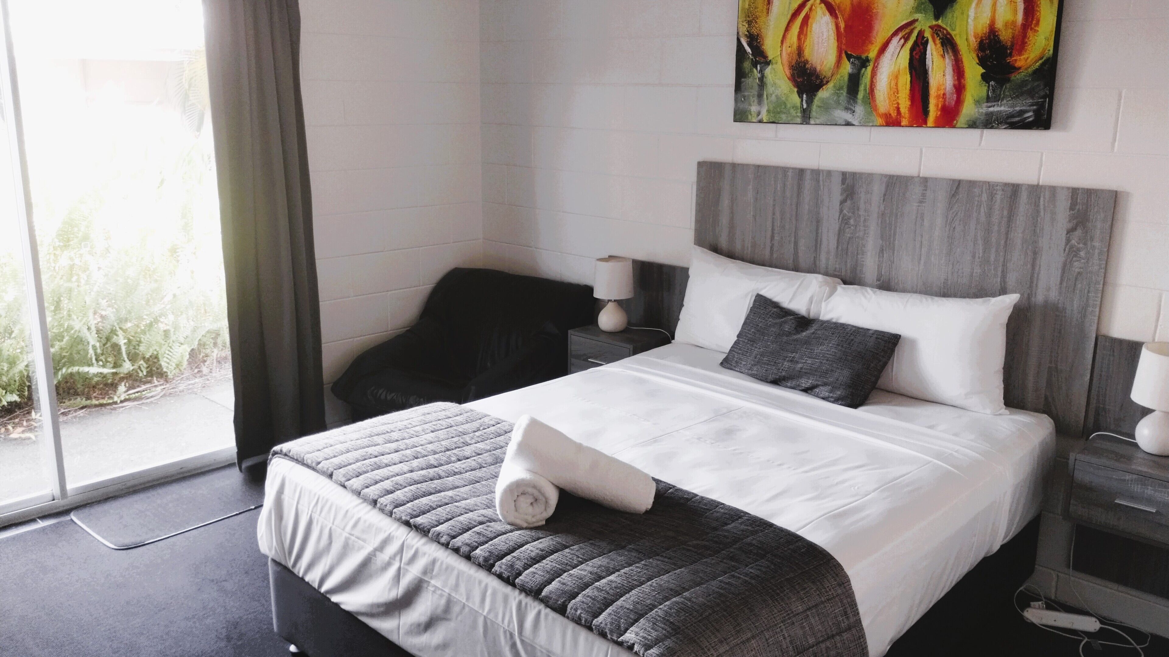 Une chambre d’hôtel avec un lit, une chaise, une table de chevet, une lampe et un tableau au mur.