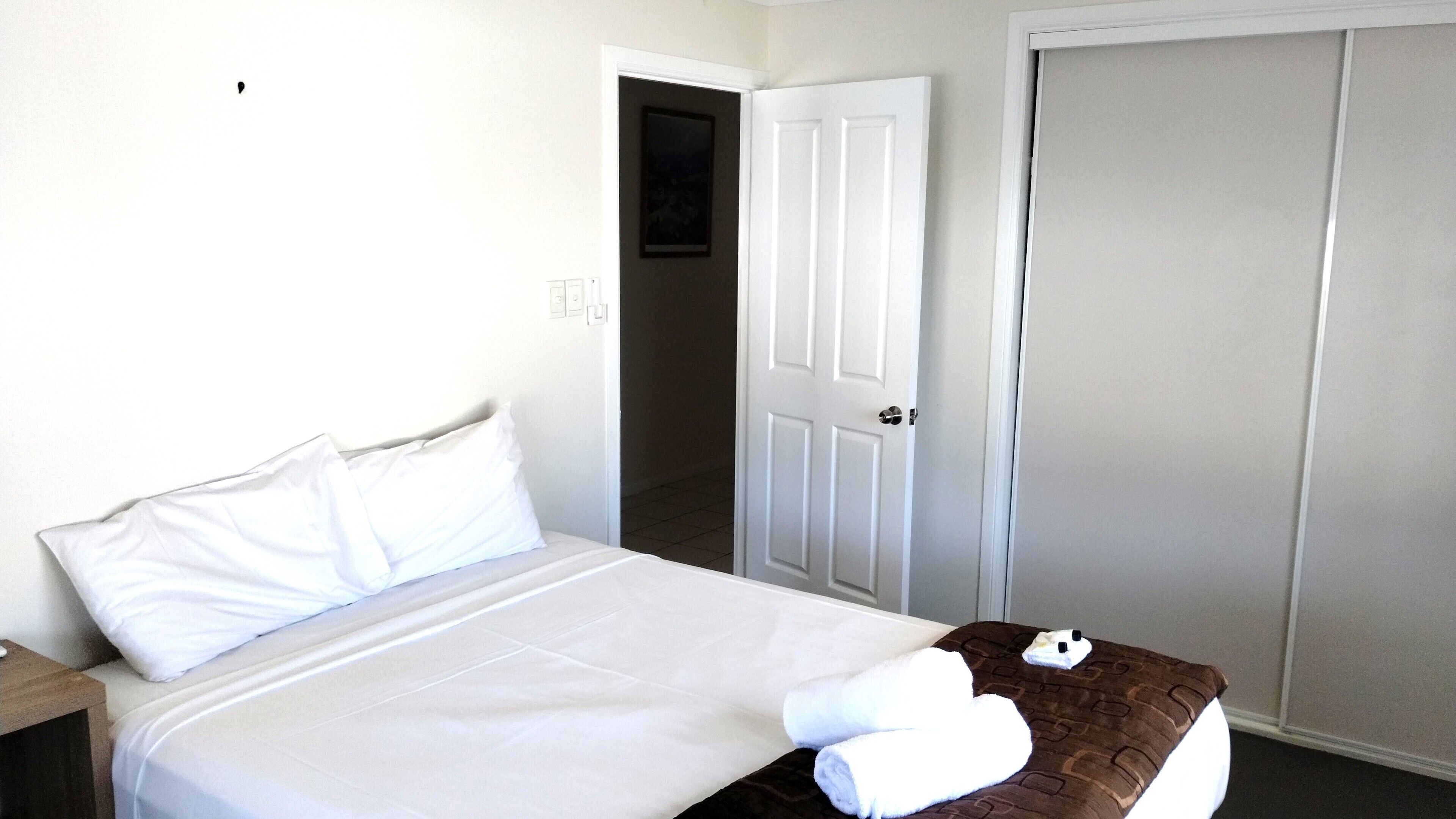 A hotel room with a bed, a nightstand, a door, and a closet.