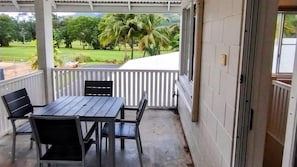 A covered outdoor area with a table and chairs, a white railing, and a view of a green landscape with trees.