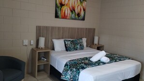 A hotel room with a wooden headboard, white bedding, a floral-patterned throw, two bedside lamps, and a painting above the bed. - Tully Motel (Tully)