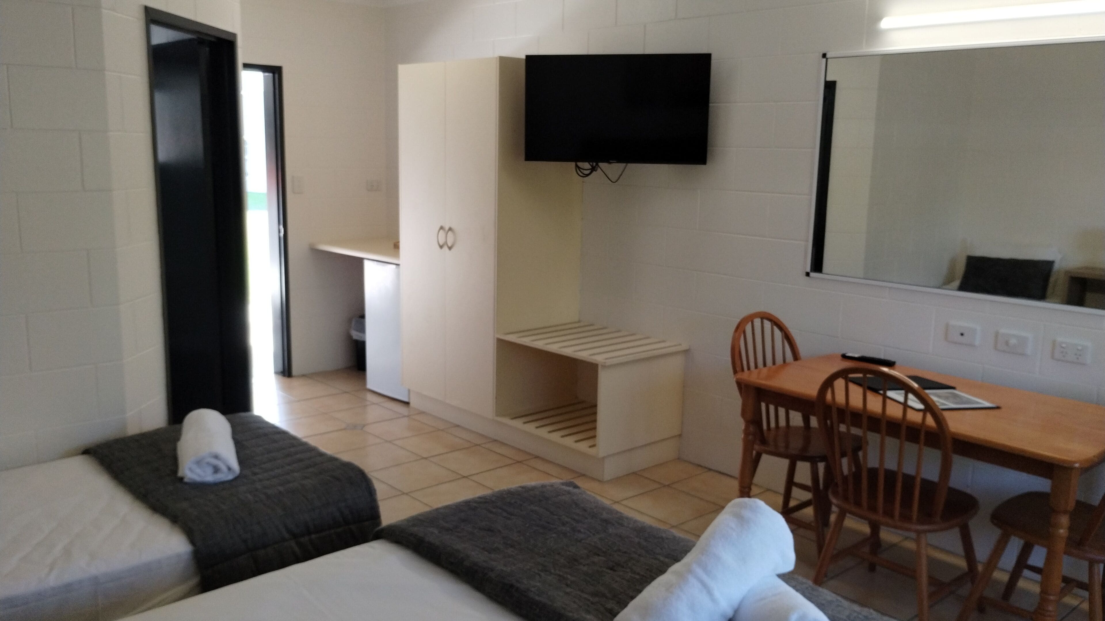 A room with two beds, a desk, a chair, a television mounted on the wall, and a small window.