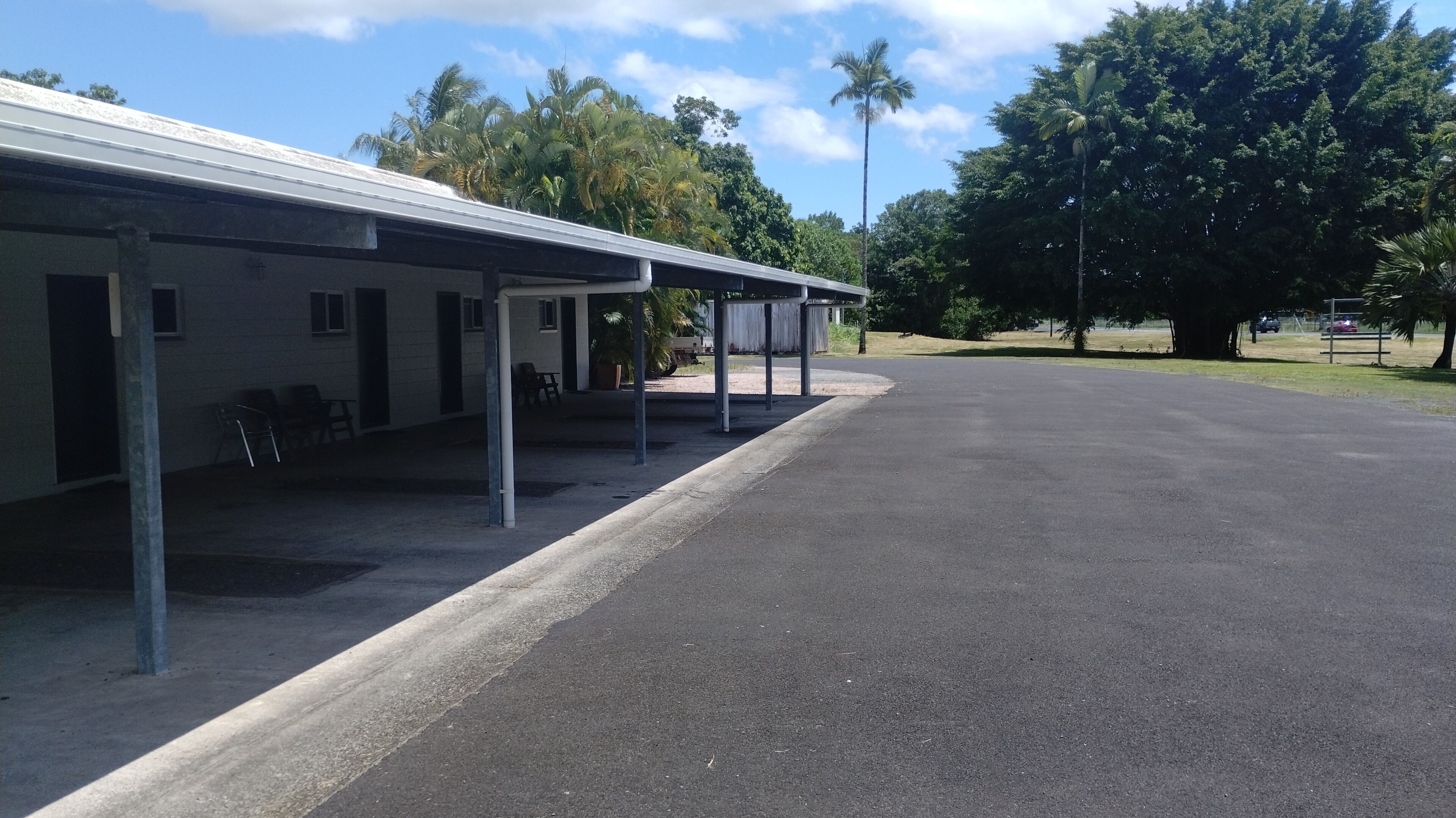 A building with a covered outdoor area, a paved driveway, and trees in the background.