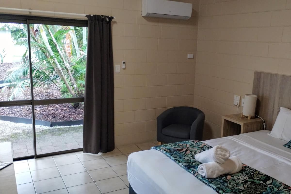 A hotel room with a bed, a chair, a nightstand, and a painting.