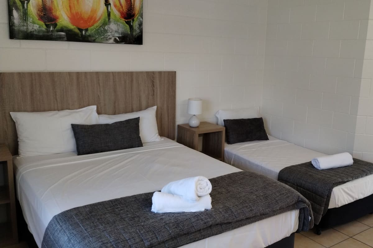 Two single beds with headboards, a nightstand with a lamp, a painting on the wall, and a shower area.