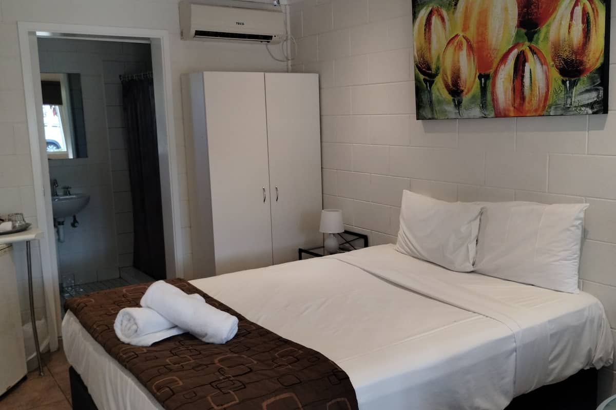 A hotel room with a bed, a wardrobe, a sink, and a painting on the wall.