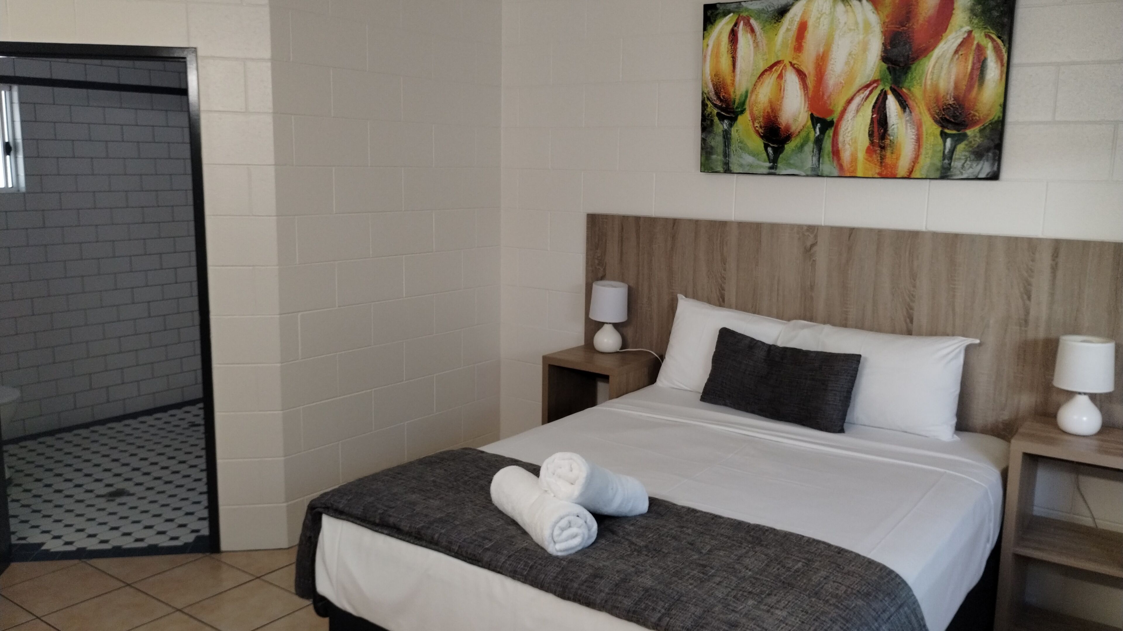 A hotel room with a bed, two nightstands, a painting, and a shower area.