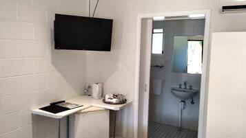 A bathroom with white tiles, a mounted TV, a sink, and a toilet.