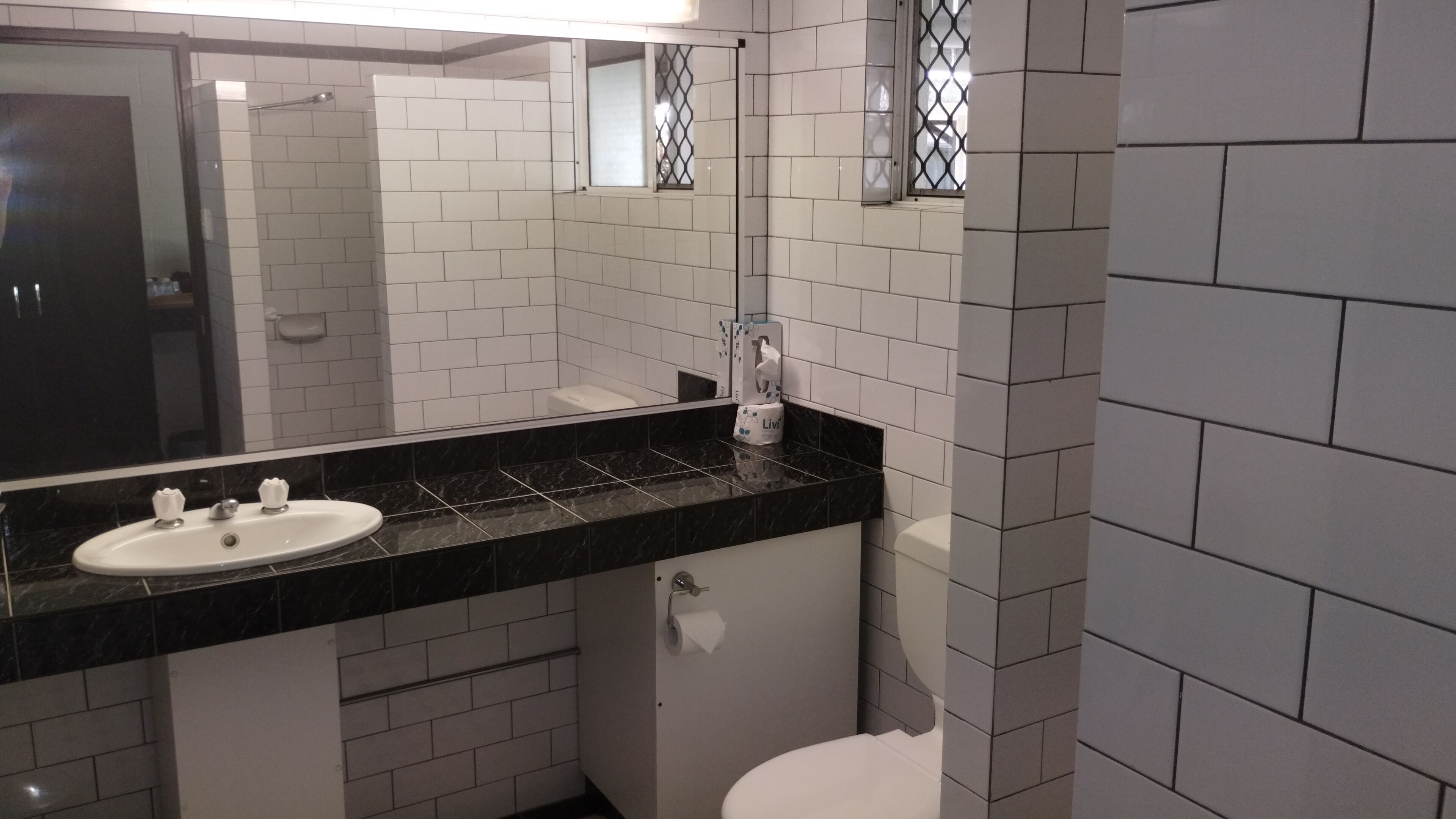 Un baño con lavamanos blanco, encimera negra y paredes cubiertas de azulejos blancos.