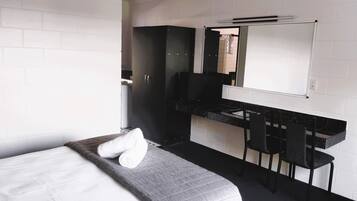 A modern hotel room with a bed, a black desk, a chair, a mirror, and a white tiled wall.