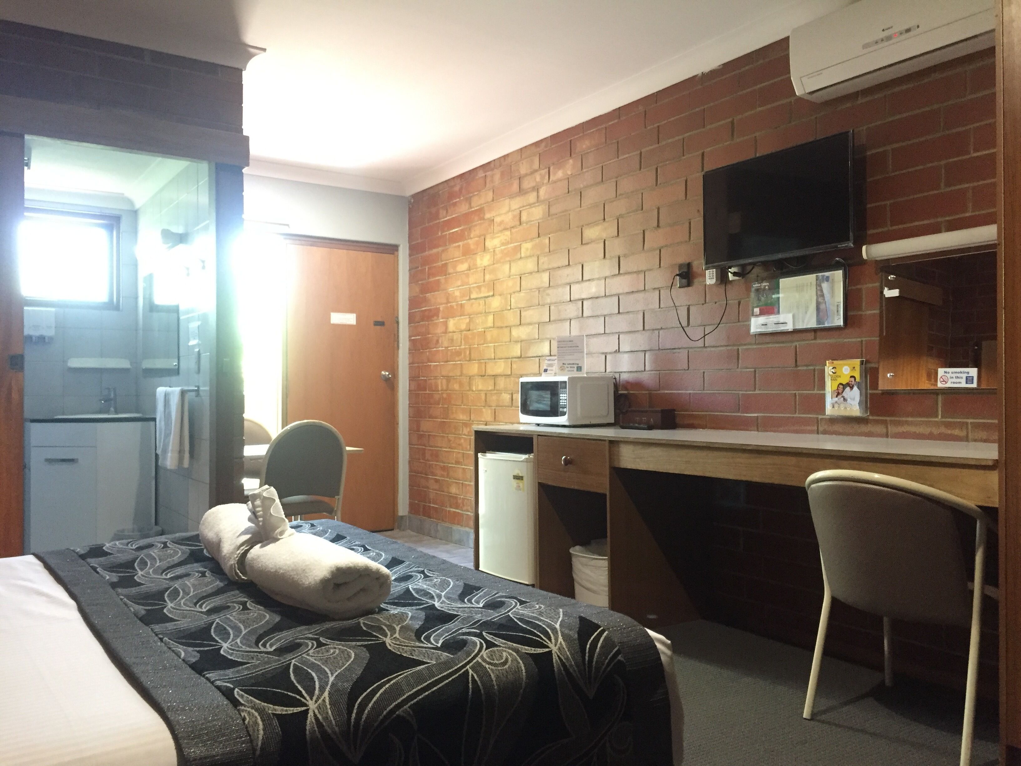 Camera d'albergo con un letto, una scrivania, un forno a microonde, una televisione e un muro in mattoni.