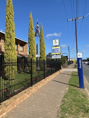 Welcome to Pooraka Motel, a peaceful retreat surrounded by a well-manicured lawn and a black fence.