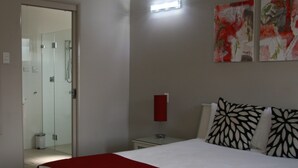 Hotelkamer met een bed, nachtkastje met lamp, douchegedeelte en twee abstracte schilderijen aan de muur.