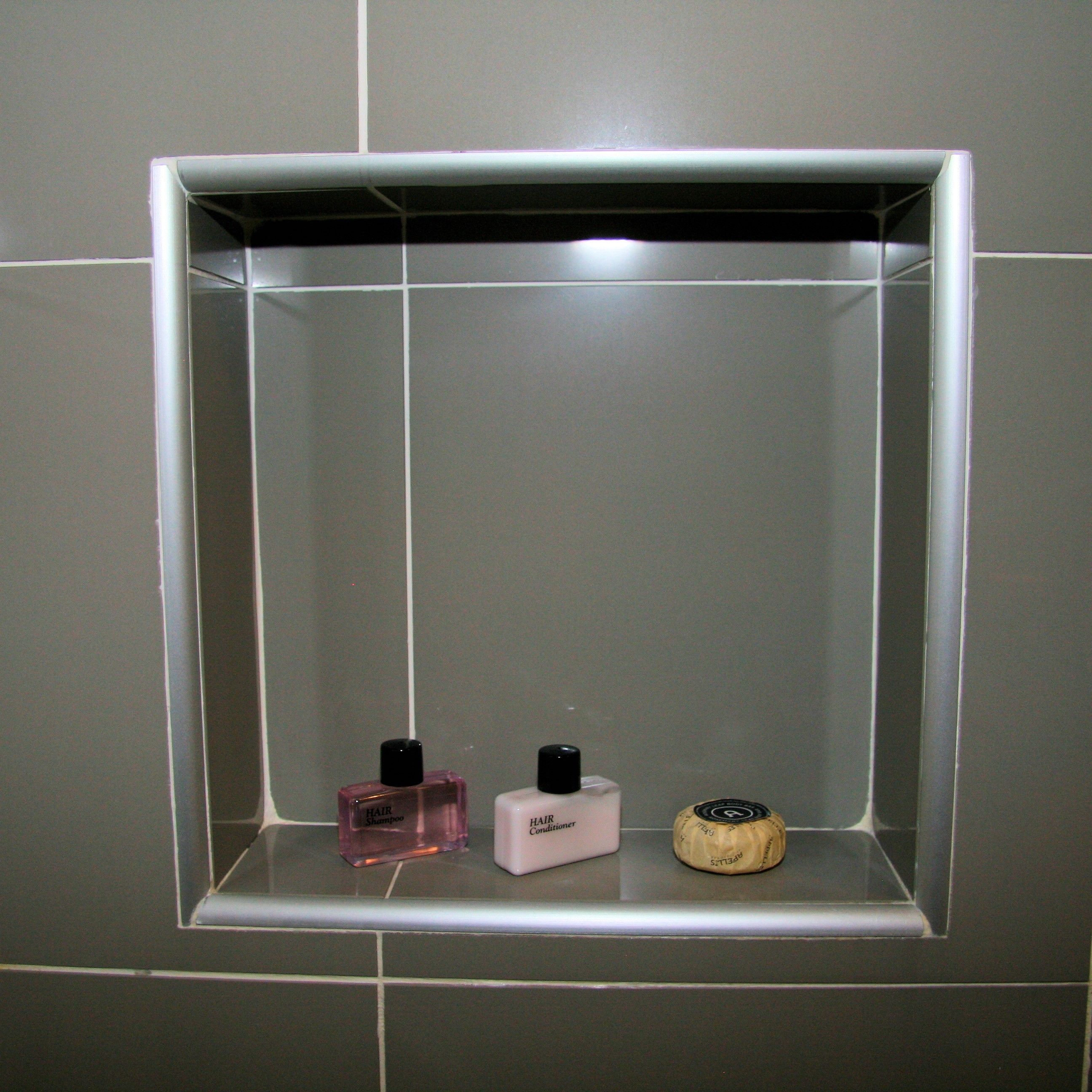 Un baño con pared de azulejos y estante que contiene tres artículos de tocador: una botella rosa etiquetada "Hair Shampoo", una botella blanca etiquetada "Hair Conditioner" y un pequeño recipiente redondo con tapa negra.