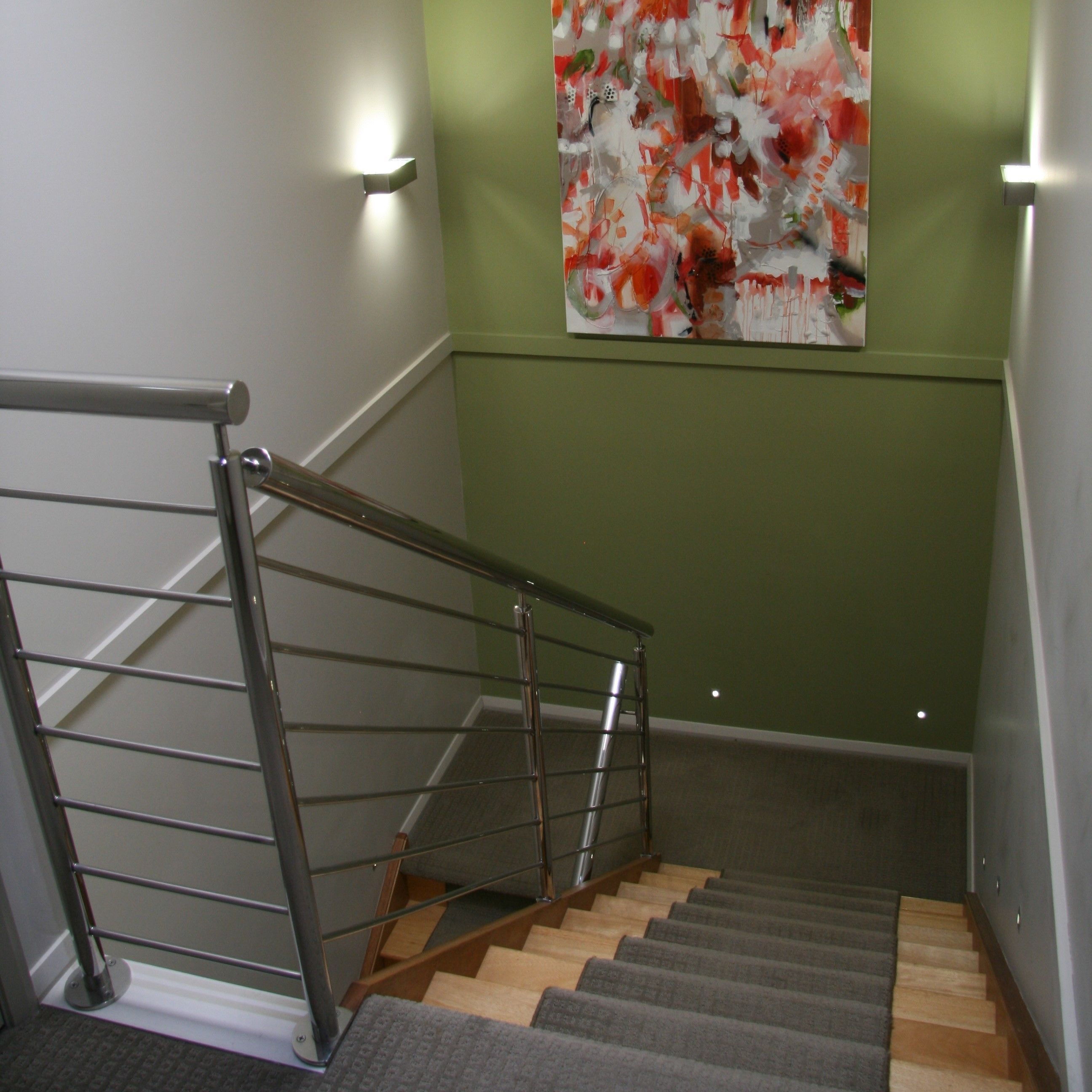 Una escalera con barandilla de metal, peldaños de madera y pared verde.