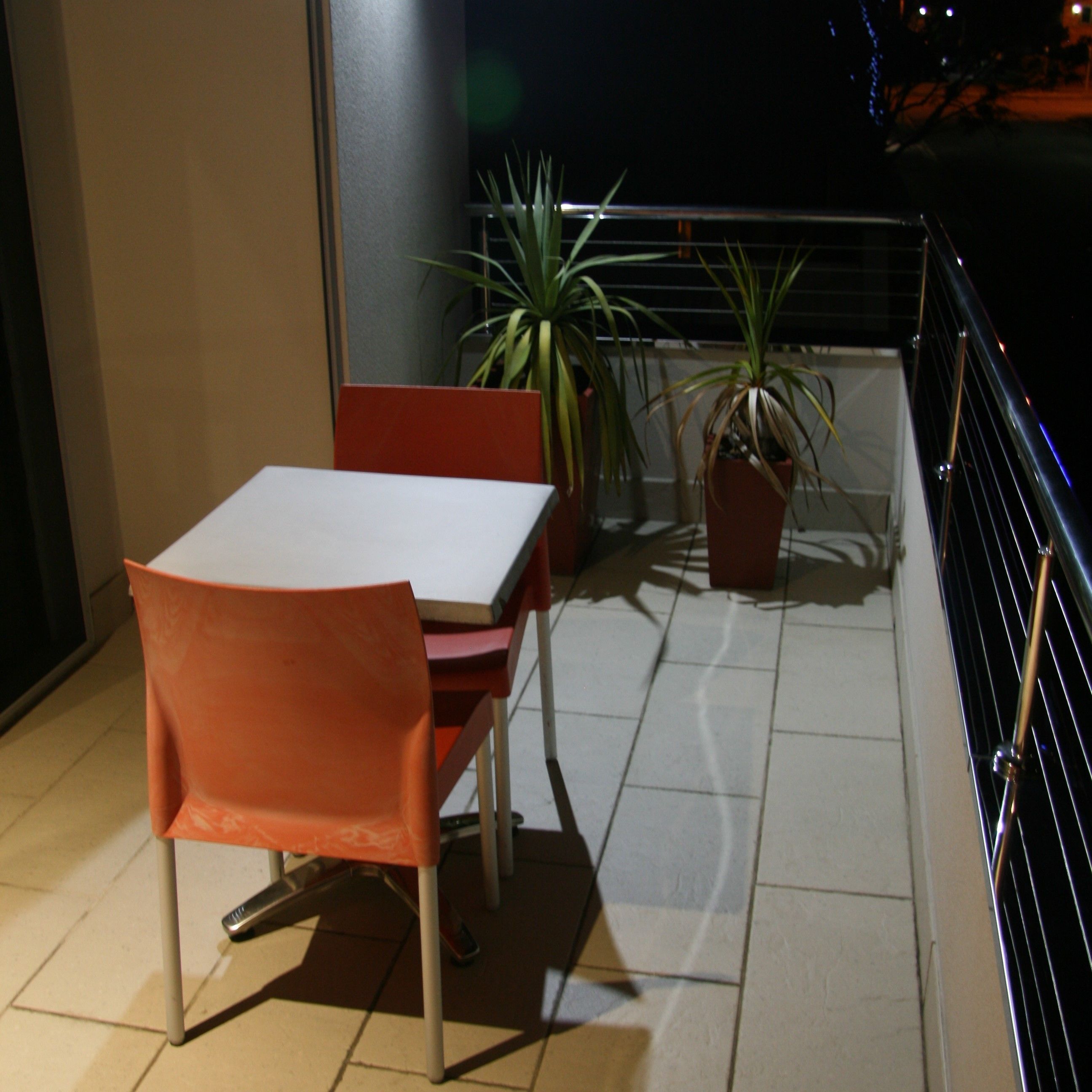 Un balcon avec une table et des chaises, des plantes en pot et une rambarde.