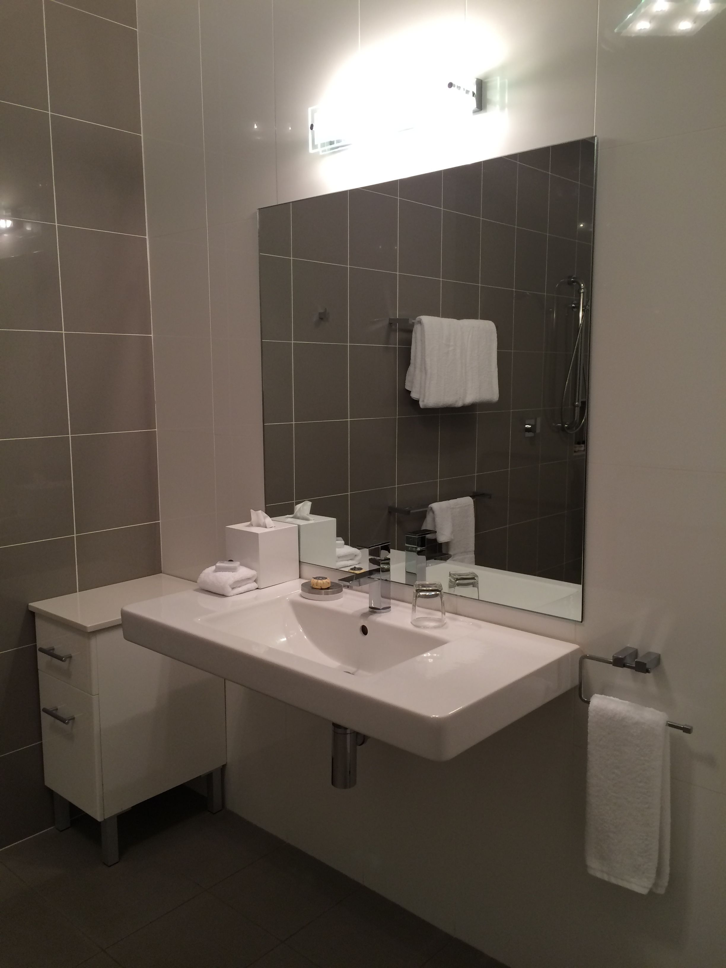 A modern bathroom with a large sink, mirror, and towel rack.