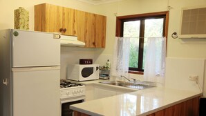 A kitchen with wooden cabinets, a white refrigerator, a microwave, a stove, and a window with lace curtains.