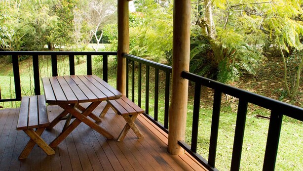 A wooden deck with a picnic table and a railing overlooking a garden with various trees and shrubs.