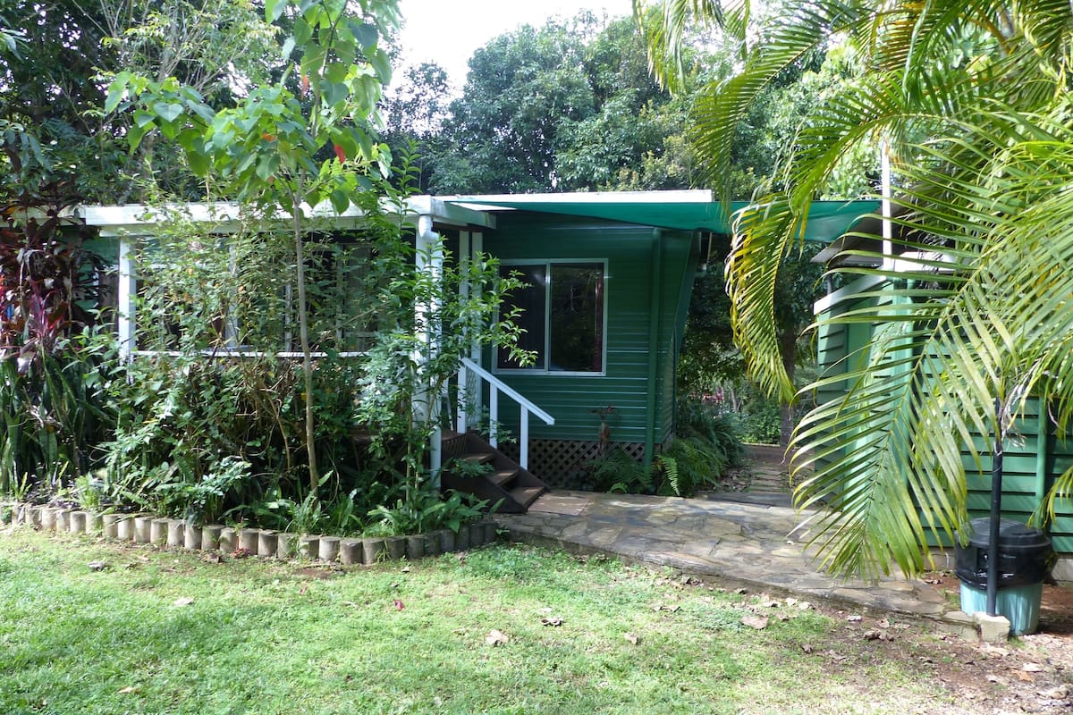 Een klein, groen huis met een veranda en treden die naar een deur leiden.