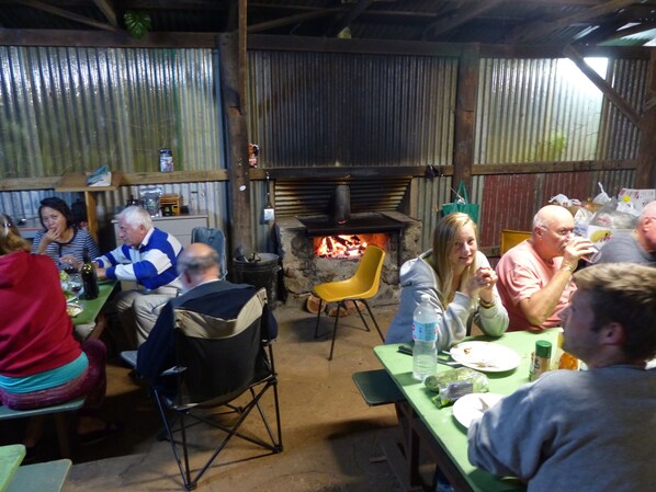 A rustic dining area with a stone fireplace, metal walls, and a mix of seating including chairs and a dining table. - Lake Eacham Tourist Park & Self Contained Cabins (Lake Eacham)