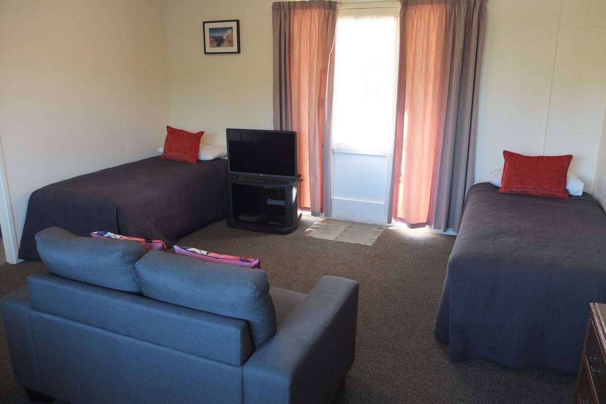 A hotel room with two beds, a TV, a sofa, and a window with curtains.