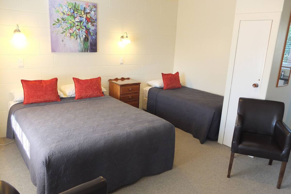 A hotel room with two beds, a wooden nightstand, a chair, and a painting on the wall.