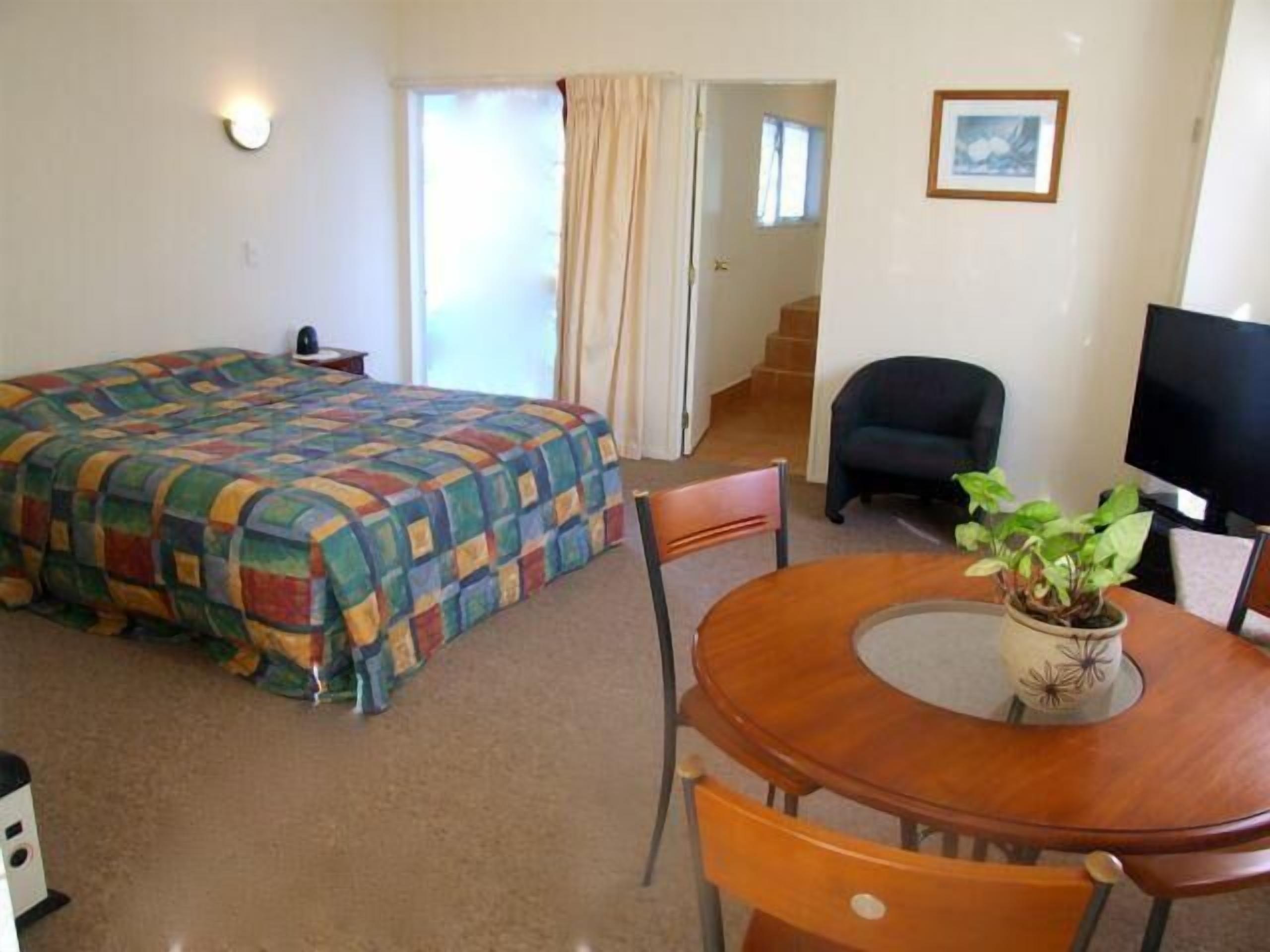 A hotel room with a bed, a desk with a chair, a television, and a potted plant.
