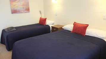 Een kamer met twee bedden, elk met een donkerblauwe sprei en een rode kussen. Er hangt een schilderij aan de muur en de muur is van wit baksteen.