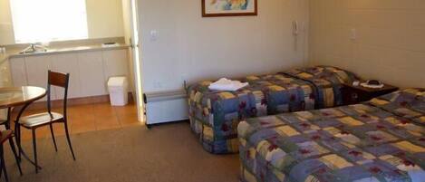Ein Zimmer mit zwei Betten, einem kleinen Tisch und einem Stuhl. Es gibt eine Küchenzeile mit einem Spülbecken und einem Fenster.