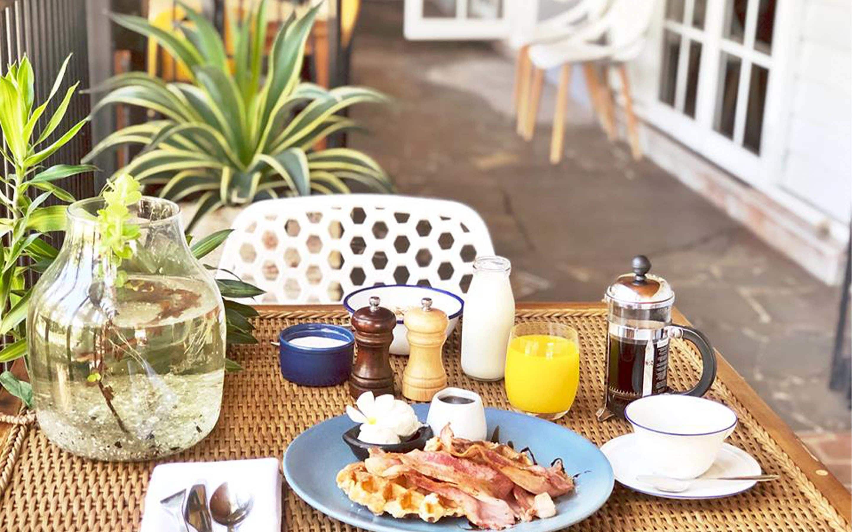 A breakfast setup with bacon, eggs, toast, and juice on a wicker table.