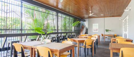 A restaurant with wooden tables and chairs, large windows, and ceiling fans.
