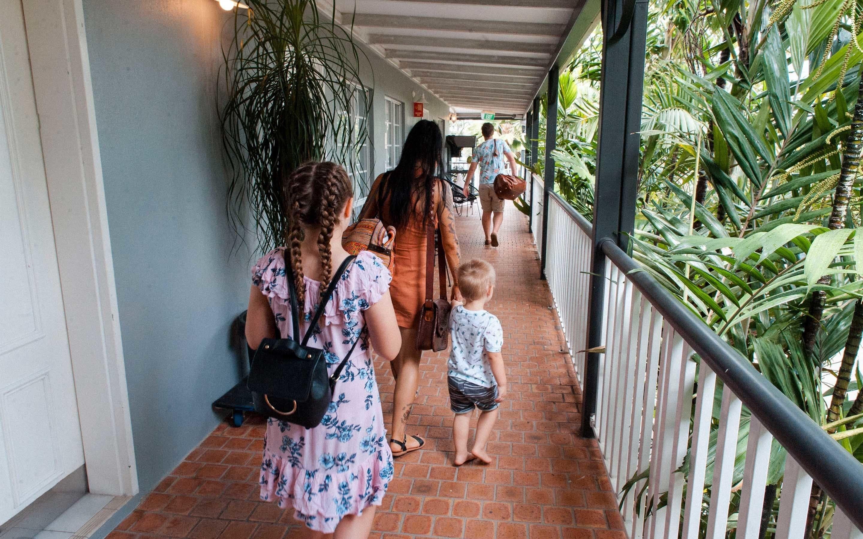 A covered walkway with a brick floor, surrounded by lush greenery and a metal railing.