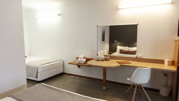 A hotel room with a bed, a desk with a chair, a mirror, and a small table with towels and mugs.