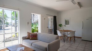 Un salon moderne comprenant un canapé, une table à manger avec des chaises, un ventilateur de plafond et de grandes fenêtres donnant sur la rue.