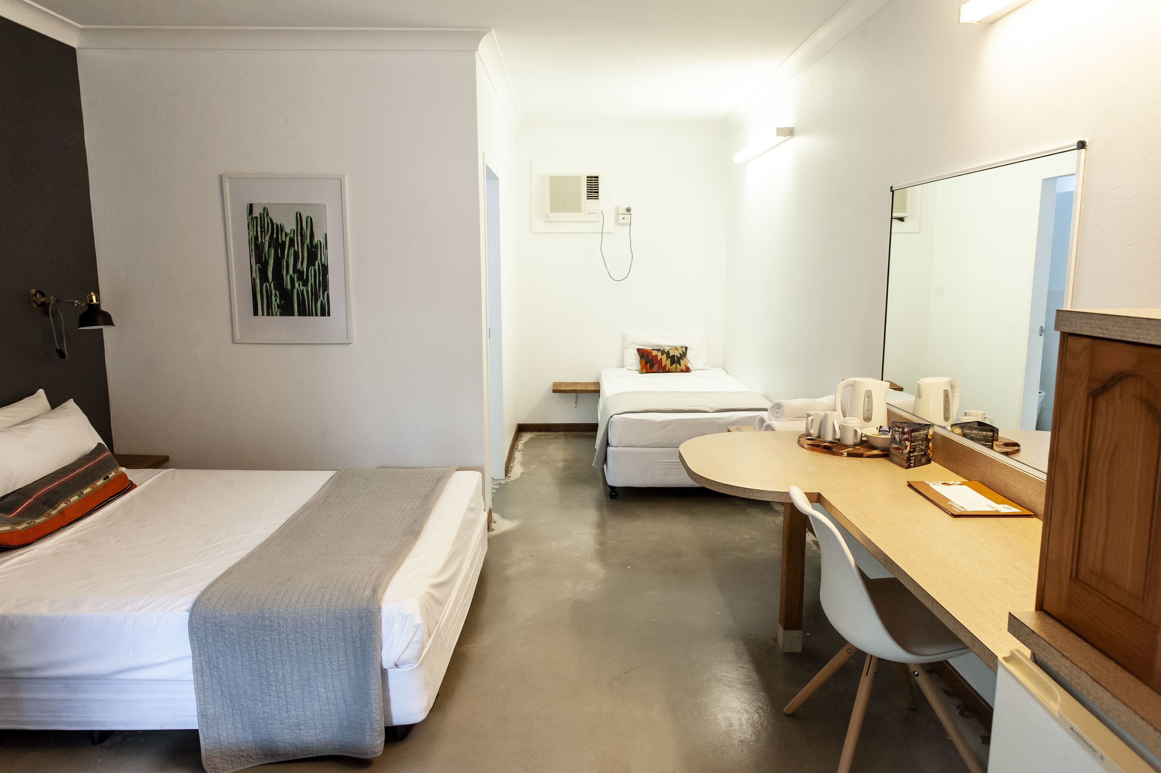 Habitación de hotel con dos camas, un escritorio, una silla, un espejo, una mesita de noche y un aire acondicionado de pared.