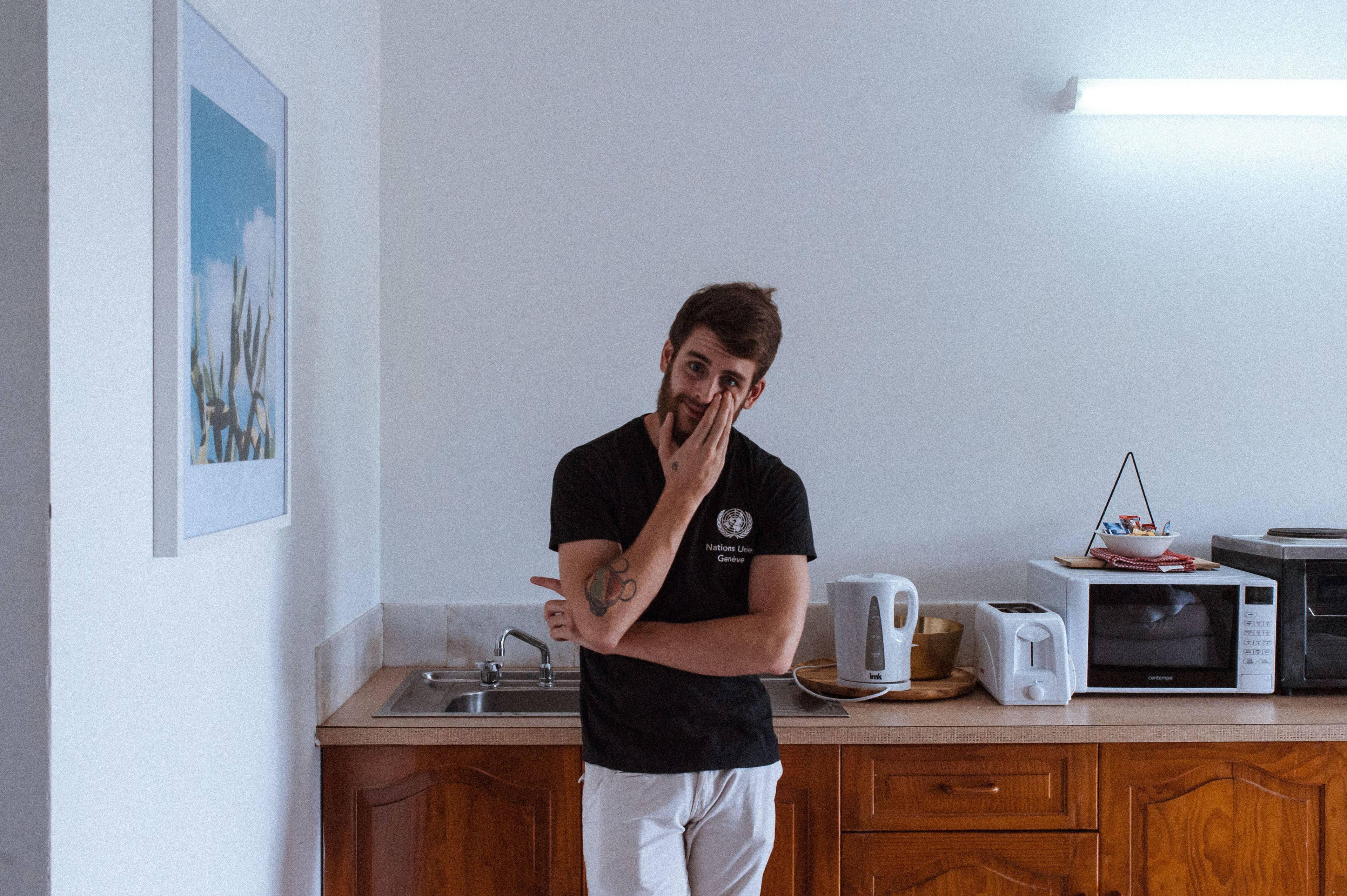 A person standing in a kitchen with wooden cabinets, a microwave, a toaster, and a kettle on the counter.