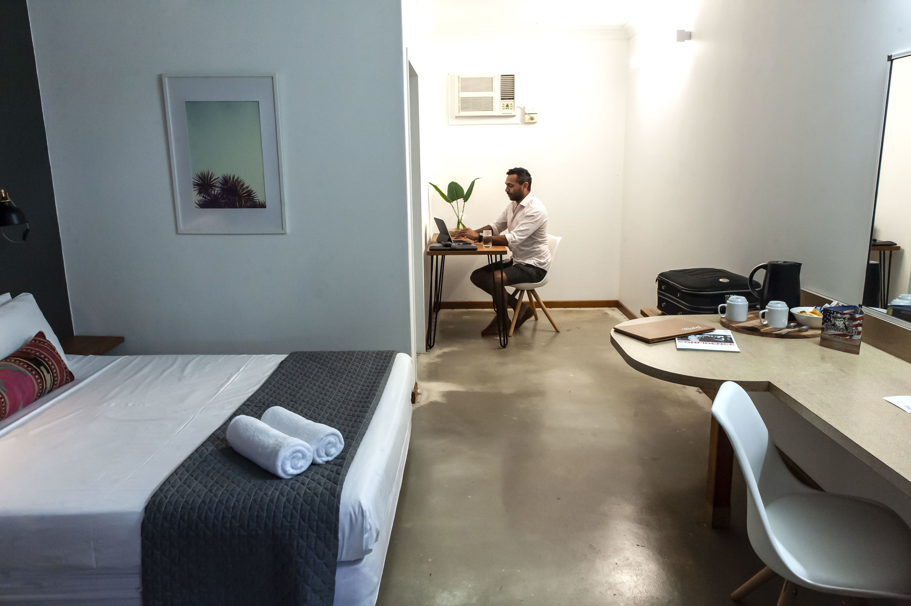 A hotel room with a bed, a desk, a chair, a coffee maker, and a plant.