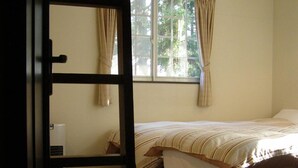 A bedroom with a bed, a window with curtains, a radiator, and a wooden ladder. - Sunny Side Hut (Hakuba)