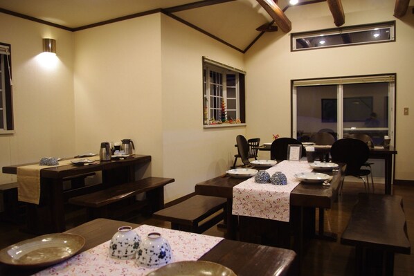 A dining area with wooden tables and benches, a small window, and a wall-mounted light fixture. - Sunny Side Hut (Hakuba)