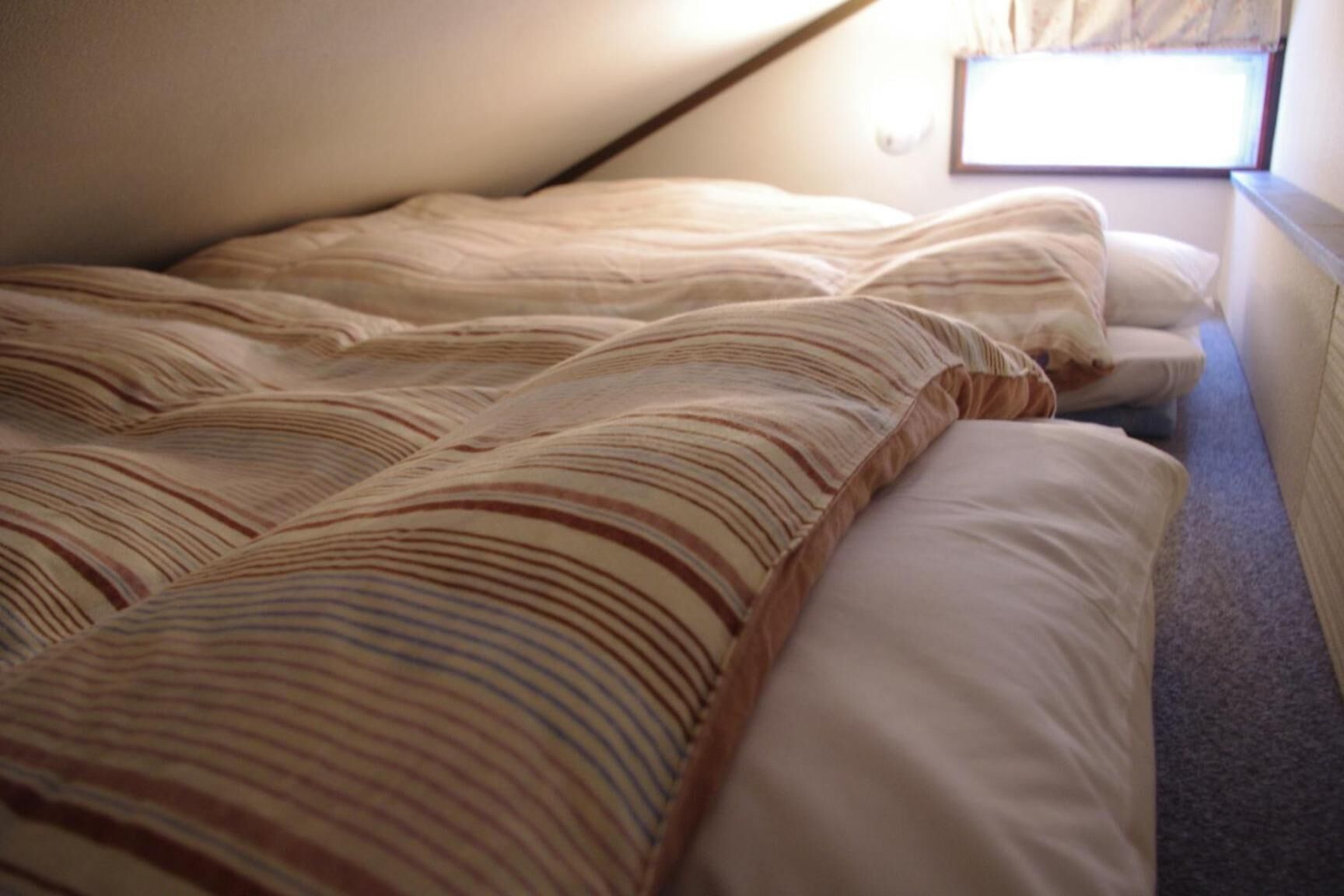 Una cama con ropa de cama a rayas en una habitación con techo inclinado y ventana.