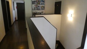 A hallway with a reception desk, a fire extinguisher, and a wall-mounted shelf with various items. - Sunny Side Hut (Hakuba)